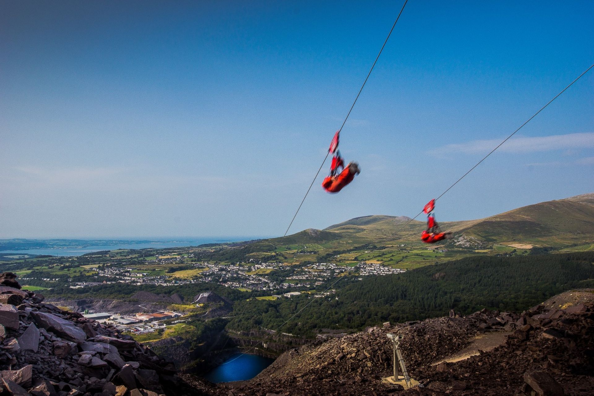 people-in-red-overalls-on-the-fastest-zip-line-in-the-world-going-over-a-quarry-in-the-mountains-north-wales-snowdonia-zip-world-adrenaline-junkie-bucket-list