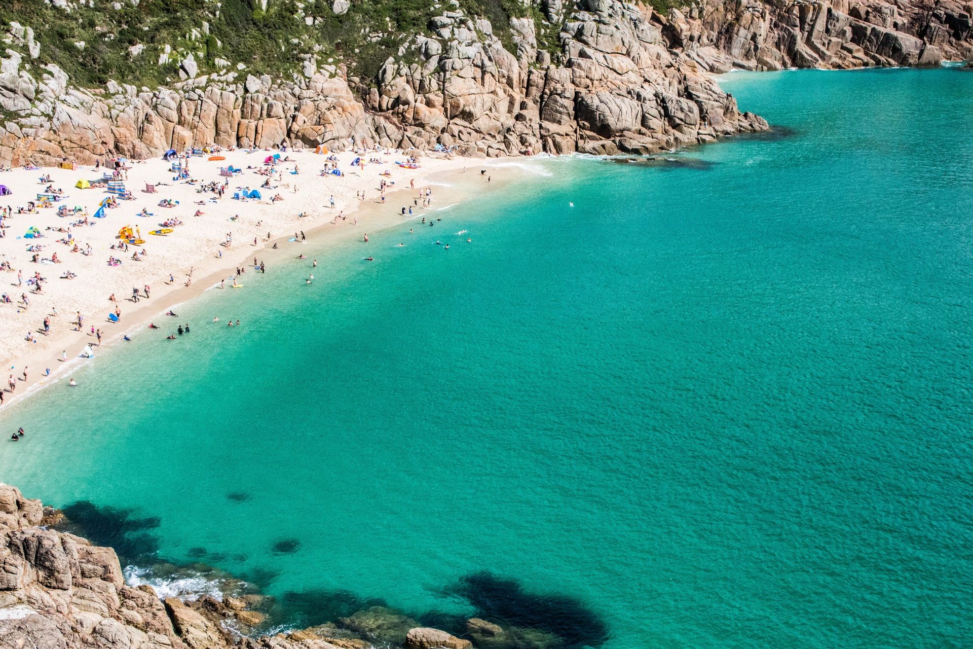 aerial-image-of-porthcurno-beach-from-above-by-minack-theatre-people-sunbathing-on-beach-beside-turquoise-waters-cornwall-hidden-gems