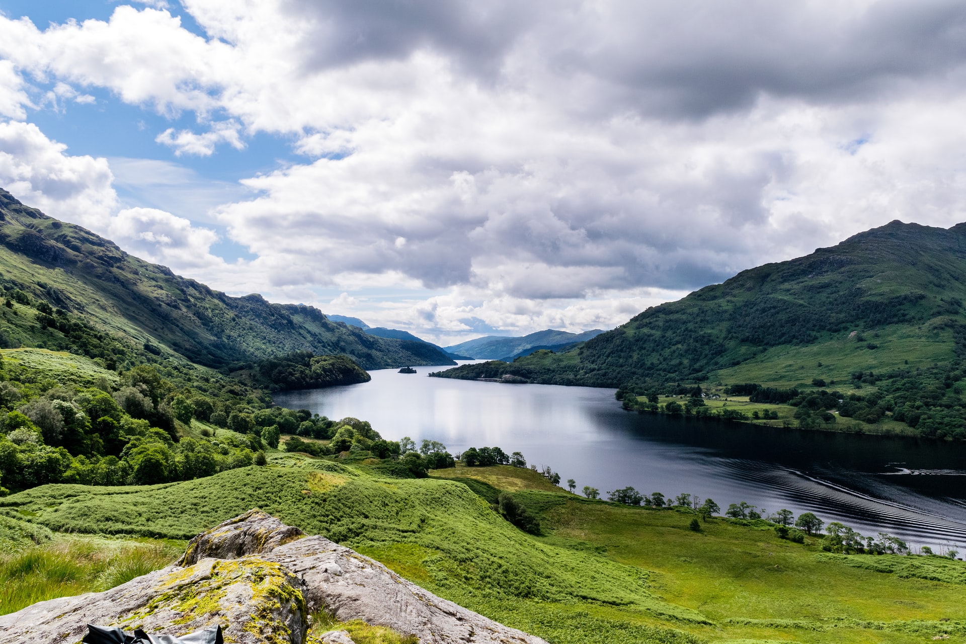 green-grass-field-near-lake-amid-mountains-under-cloudy-sky-loch-lomond-scenic-drives-in-scotland