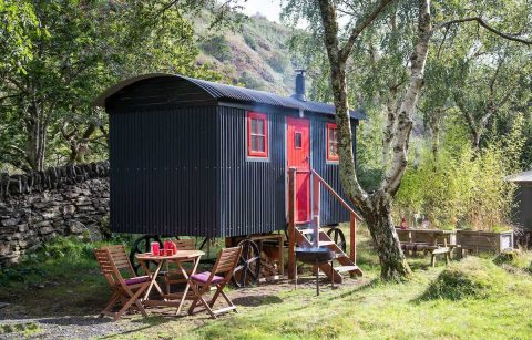 blue-and-red-shepherds-hut-in-field-with-mountains-in-background-graig-wen-glamping-snowdonia