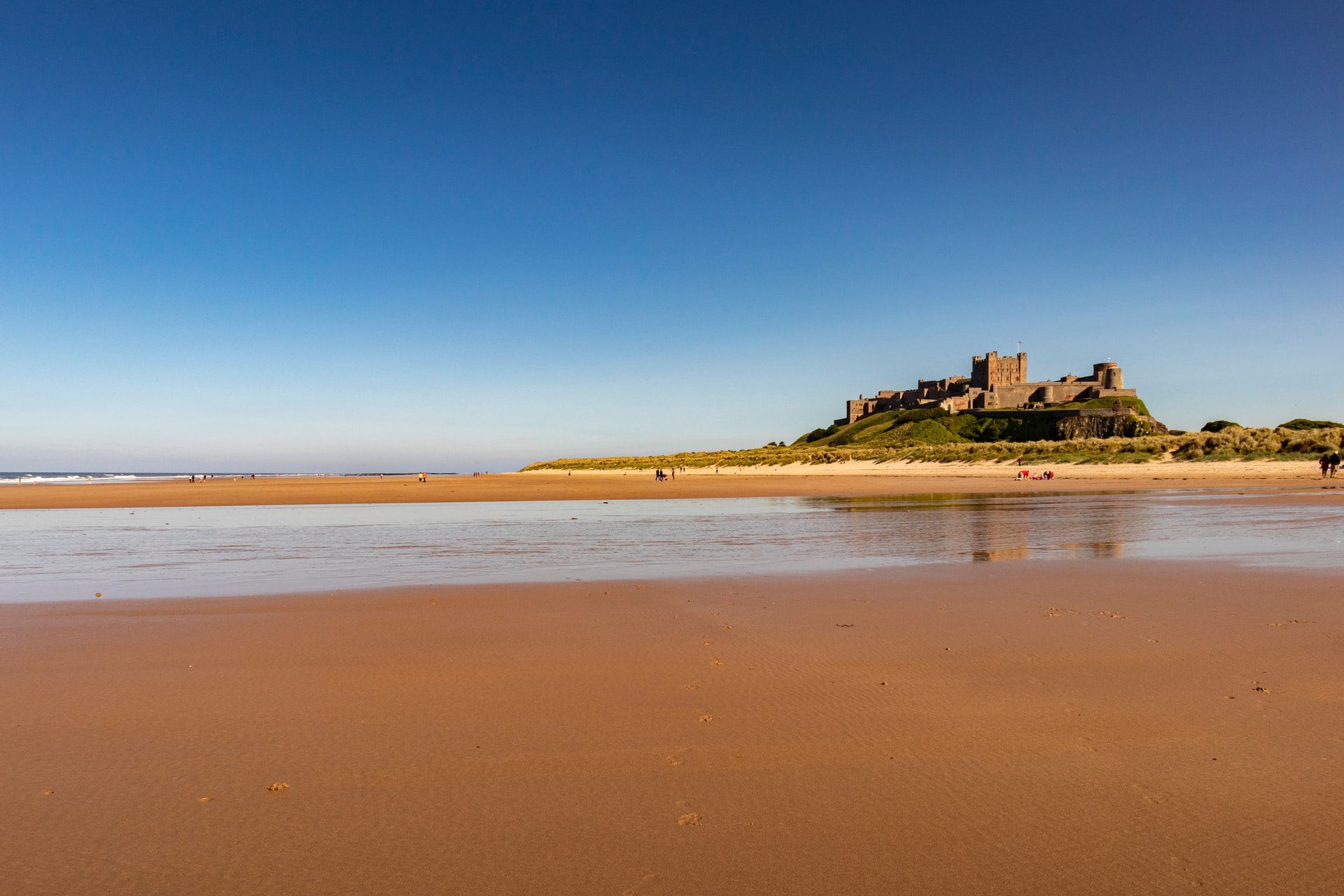 bamburgh-castle-on-hill-out-at-sea-by-sandy-beach-at-sunset-best-places-to-visit-in-northumberland