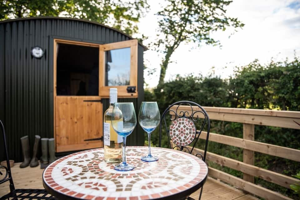 garden-table-with-glasses-of-wine-in-front-of-green-bank-shepherds-hut-in-cockermouth-airbnbs-lake-district