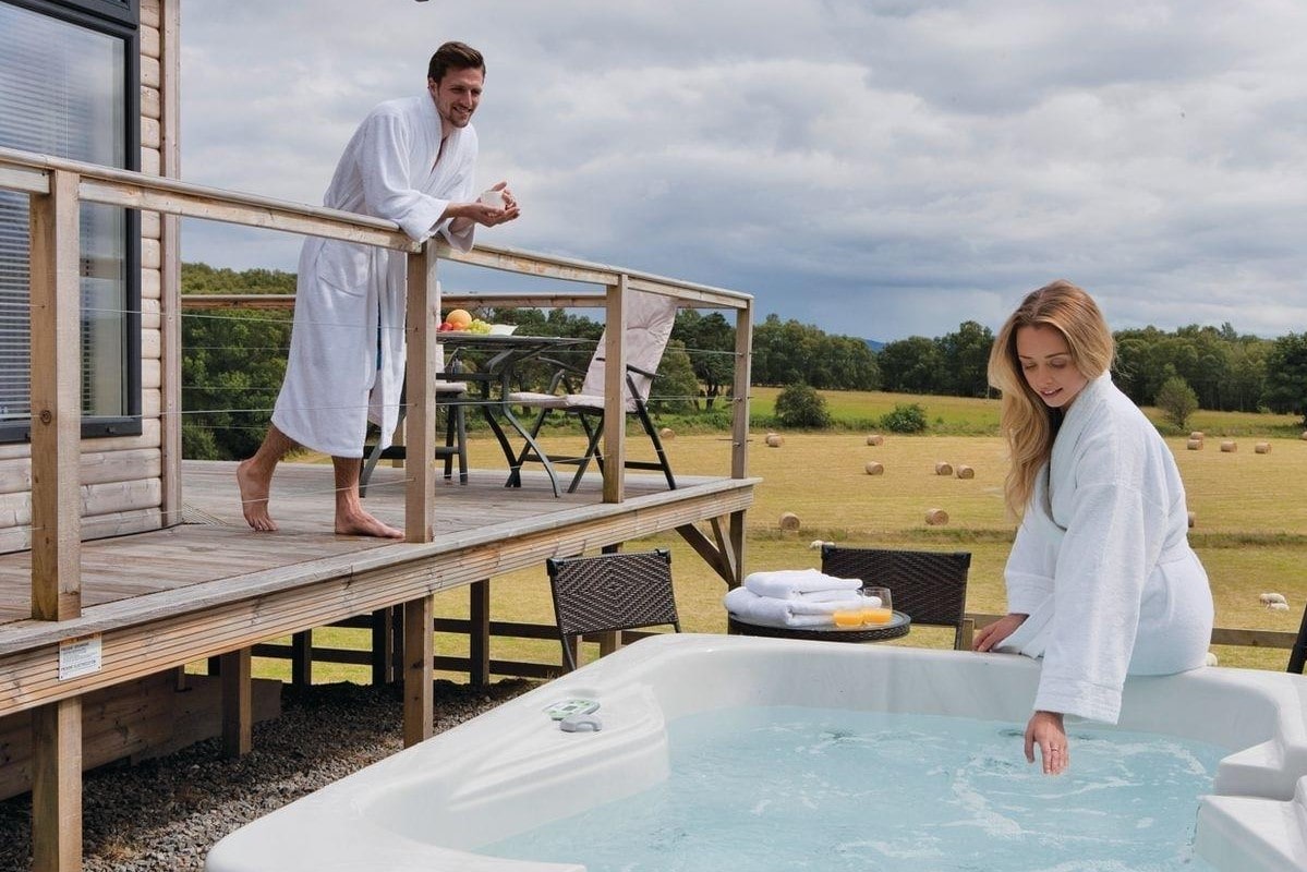 man-on-decking-and-woman-leaning-on-hot-tub-at-kessock-highland-lodges