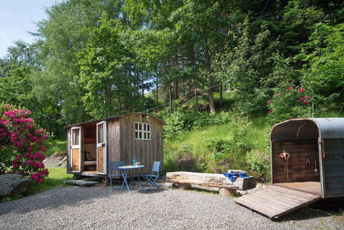 small-wooden-shepherds-hut-with-blue-seating-area-with-trees-in-background