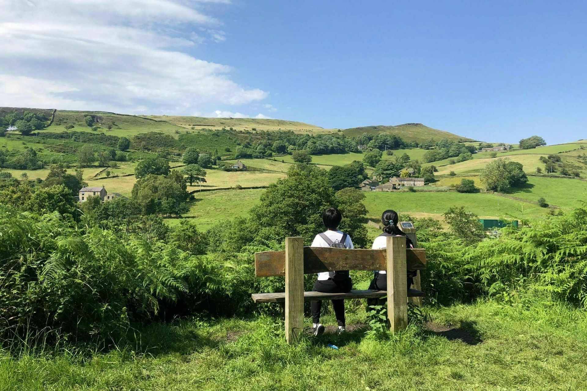 two-people-sat-on-bench-on-sunny-day-overlooking-green-countryside-on-the-sett-valley-trail