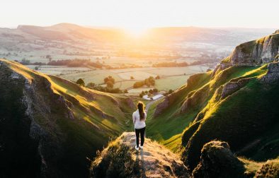 woman-standing-on-rock-overlooking-winnats-pass-winding-road-and-countryside-at-sunset-best-peak-district-walks