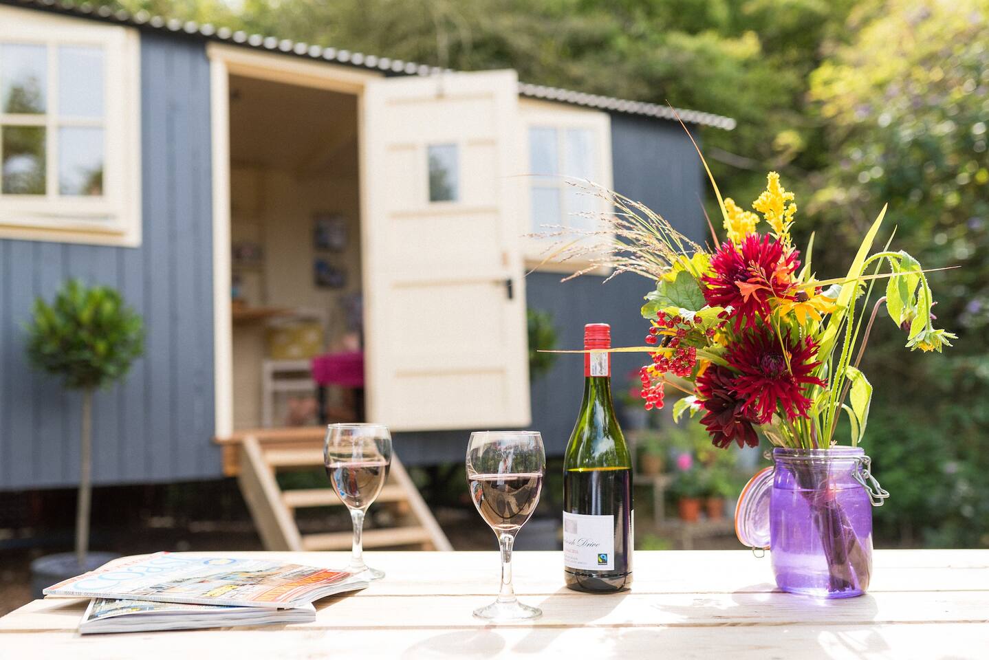 wooden-table-with-red-wine-and-flowers-in-front-of-hut-next-the-sea-shepherds-hut