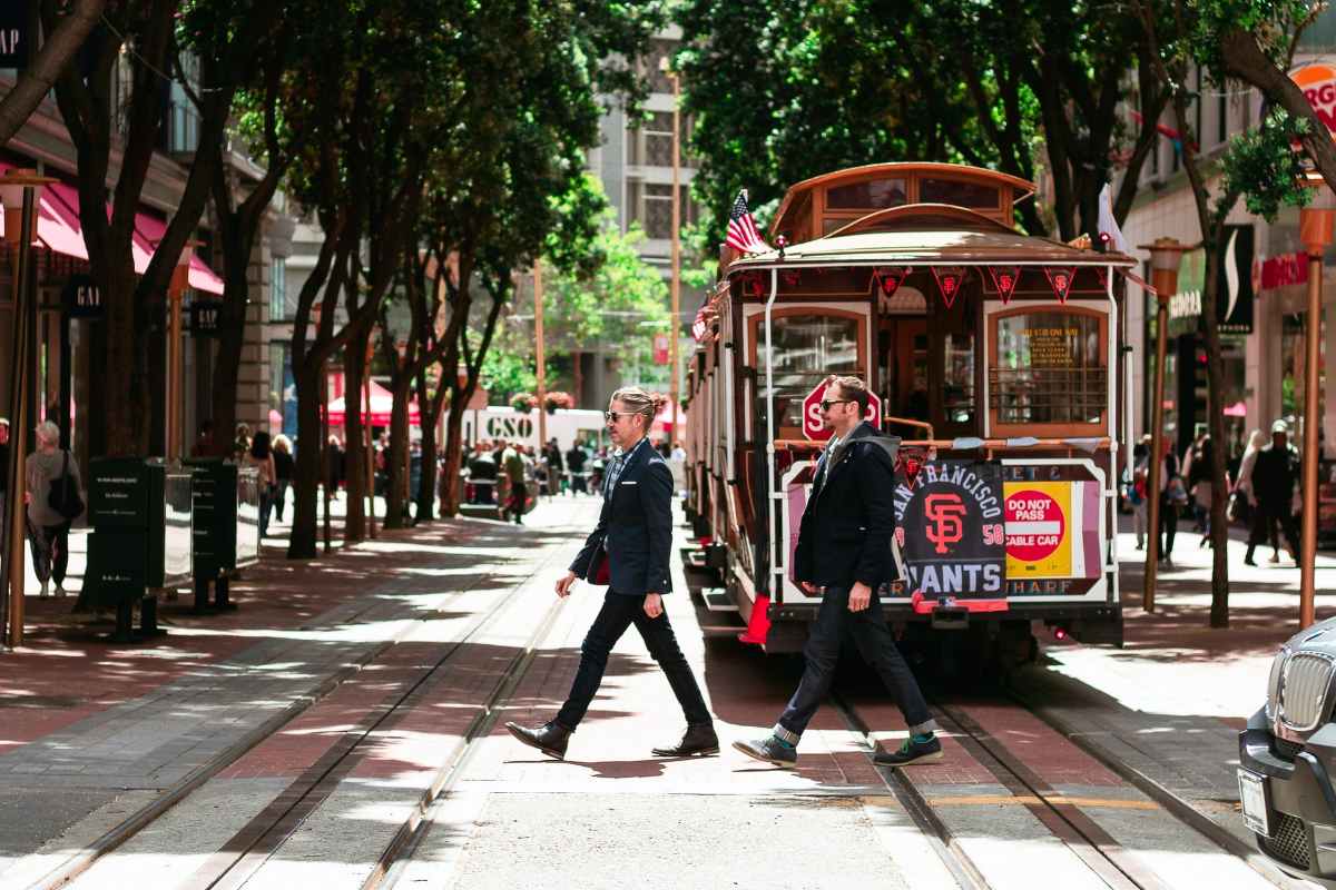 two-men-walking-across-a-tree-lined-street-past-a-tram