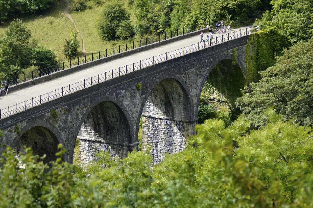 people-walking-over-bridge-viaduct-going-over-green-fields-at-monsal-trail-head