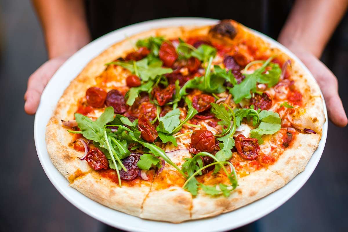 pizza-topped-with-tomatoes-and-rocket-in-hands-bath-pizza-co