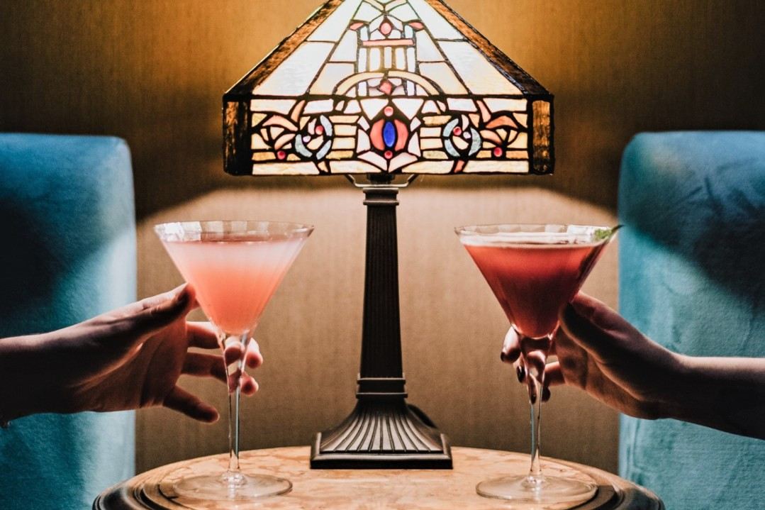 hands-holding-cocktails-by-lamp-inside-mobster-bar