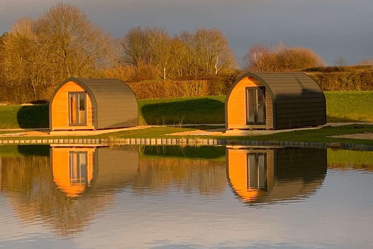 two-pods-seen-across-a-lake-at-fields-end-water-glamping-in-the-daytime